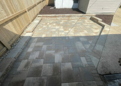 Backyard pavers with wooden fence and shadow across the middle of the photo